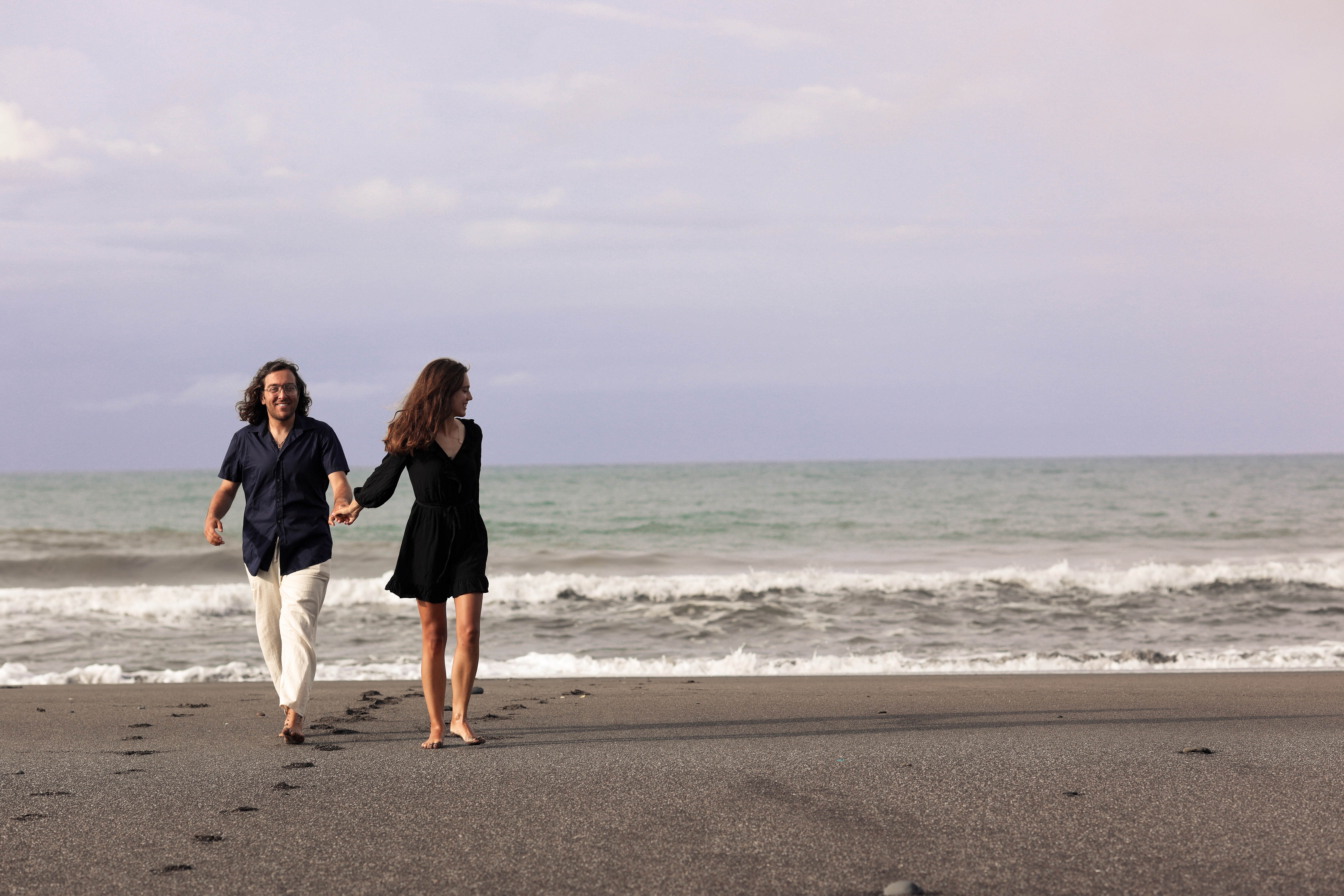 Couple walking hand in hand on a sandy beach with ocean waves in the background