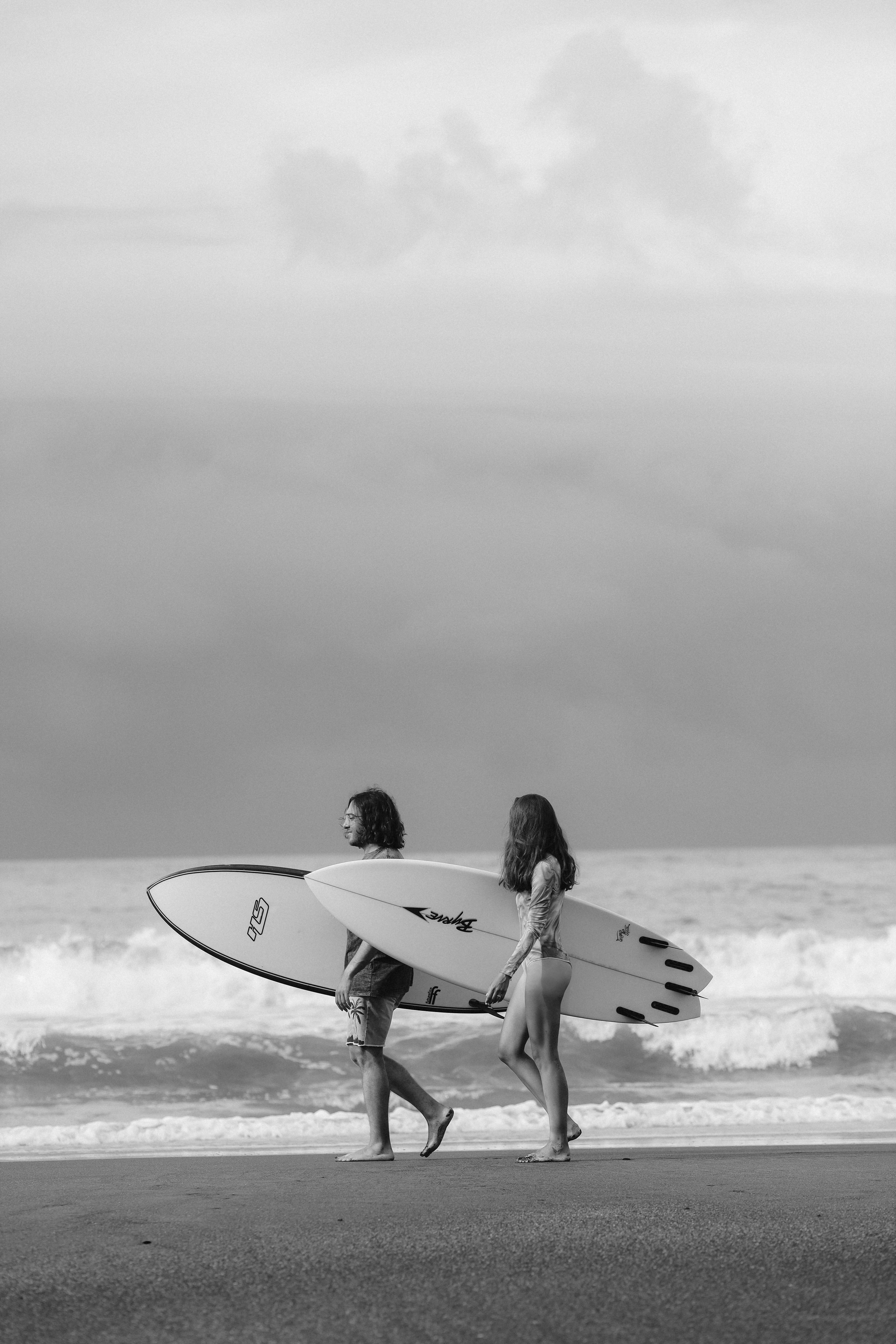 Black and white photo of a couple walking on the beach with surfboards